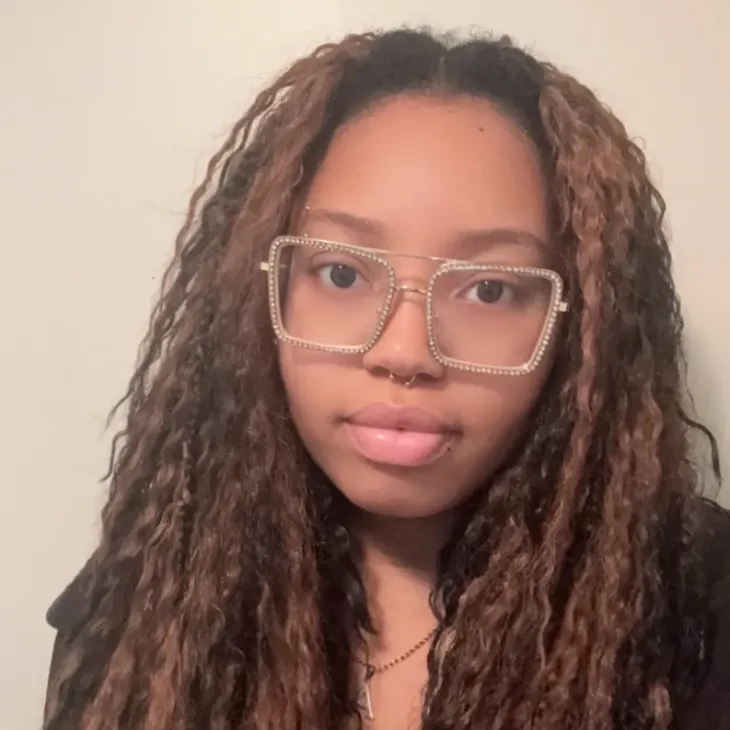 A woman with long braided hair and glasses smiles gently at the camera.