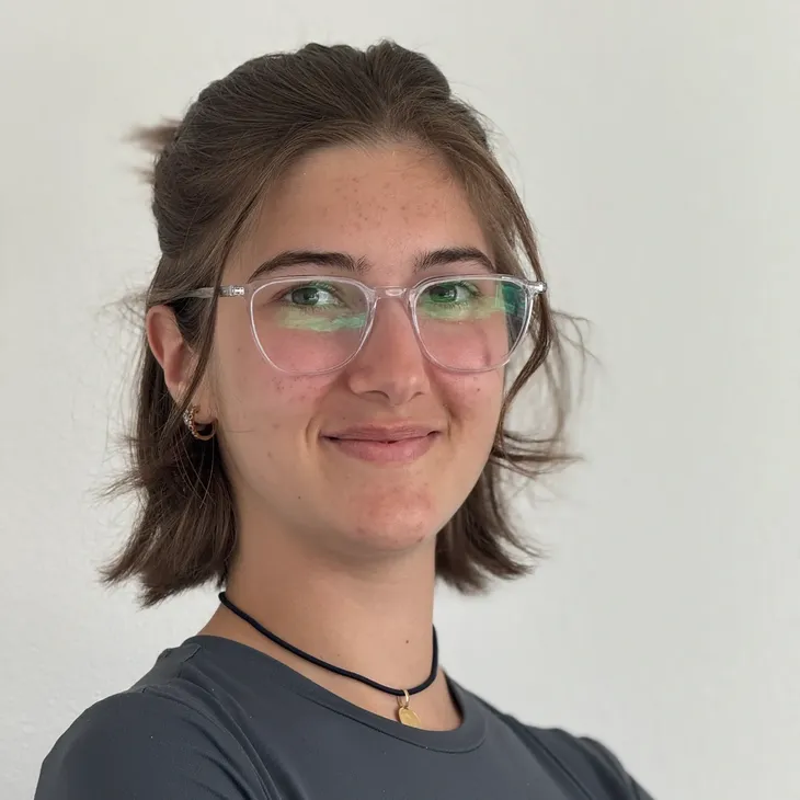 Young woman with glasses smiling confidently against a plain background.