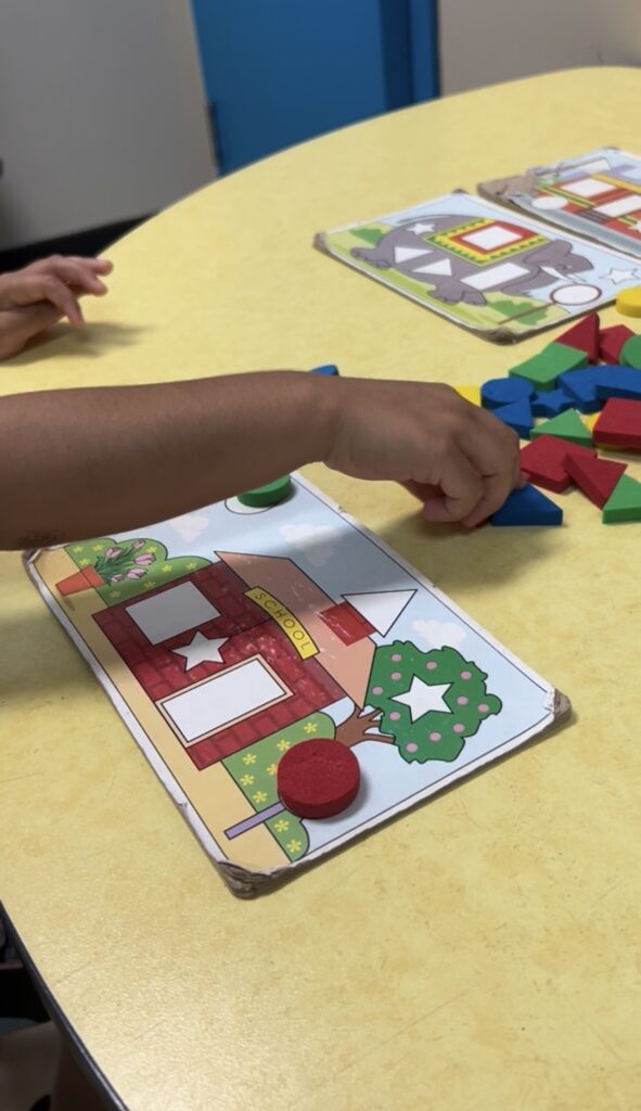 Child arranging colorful geometric shapes on a holiday-themed activity card.