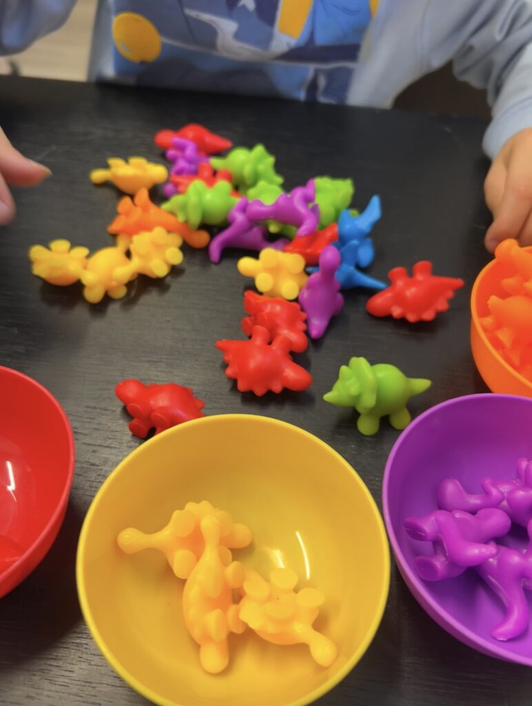 Colorful dinosaur-shaped toys scattered and grouped in bowls on a table.